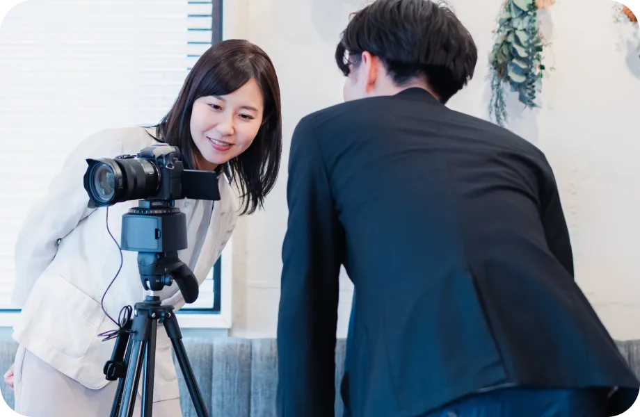 室内でカメラのモニターを覗き込む女性と男性が、撮影内容を確認している様子