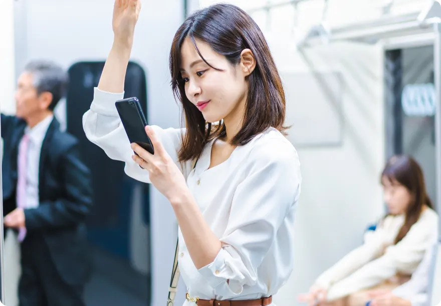電車内で若い女性が片手でつり革を持ちながらスマートフォンを操作している様子